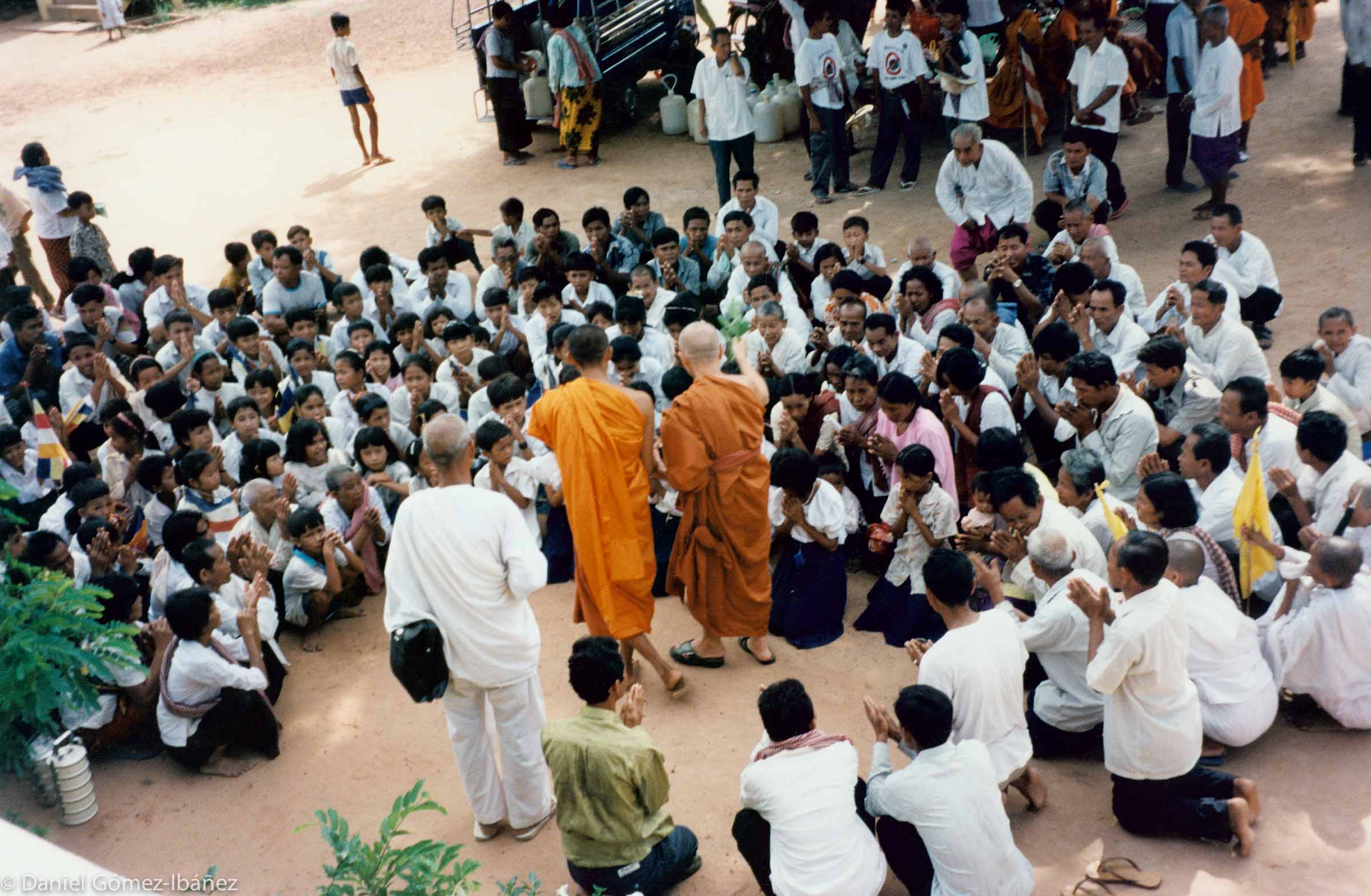 Between 1975 and 1979, the years of the Pol Pot dictatorship, about a quarter of the Cambodian population perished in Khmer Rouge killing fields, including almost all of the country's Buddhist monks. And as late as the 1990s, guerilla remnants of the Khmers Rouges continued to fight Cambodian government troops. Each year, Maha Ghosananda, the monk who almost single-handedly had restored Buddhism in Cambodia after the holocaust of the Pol Pot regime, led a month-long peace walk through heavily-mined combat zones in rural Cambodia. Maha Ghosananda is standing, center right, in the darker robe, blessing a crowd who had come to hear his dharma talk after a day of walking. Some of these villagers were seeing a Buddhist monk for the first time in many years. [near Takeo, Cambodia, 1996]